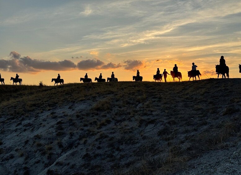Silhouettes of people riding horses on a grassy hill during sunset. 3