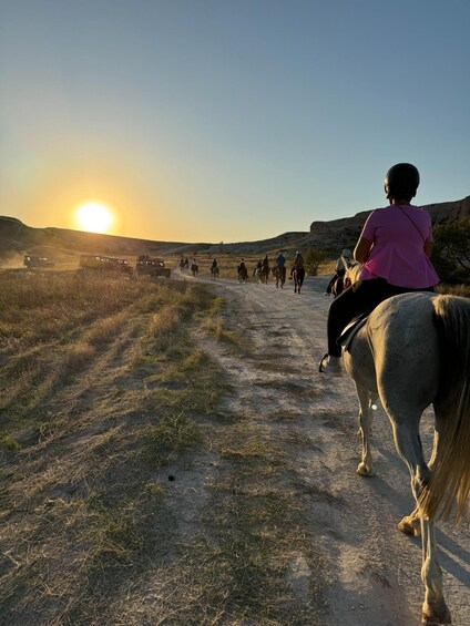 A group of people riding horses on a dirt path during sunset. 5