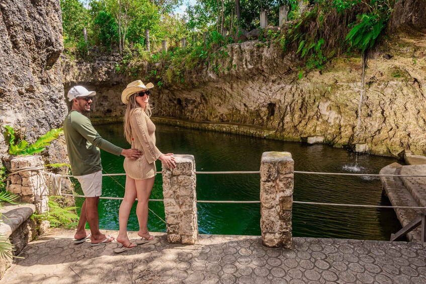 A couple standing by a stone wall overlooking a body of water with greenery and rocky terrain in the background. 5