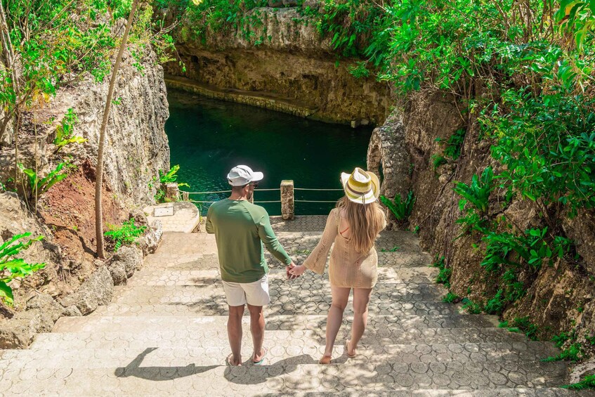A couple walking on a stone pathway towards a natural pool surrounded by greenery and rocky cliffs. 1