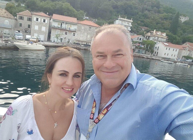 Two people on a boat with a backdrop of stone buildings and a body of water. 1