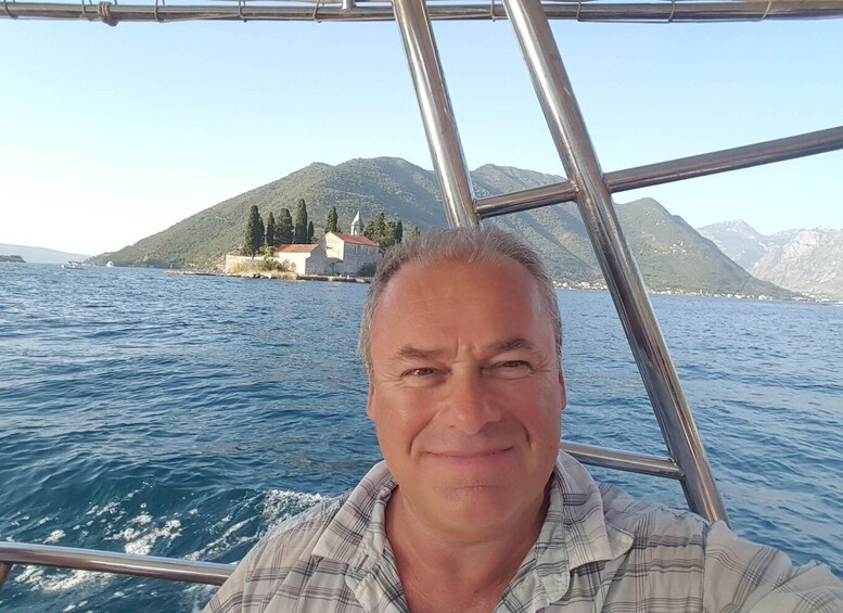 A man on a boat with a mountainous landscape and a small building in the background. 1