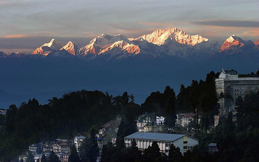 A mountain range with snow-capped peaks, a town with buildings, and a large white building on a hill. 2
