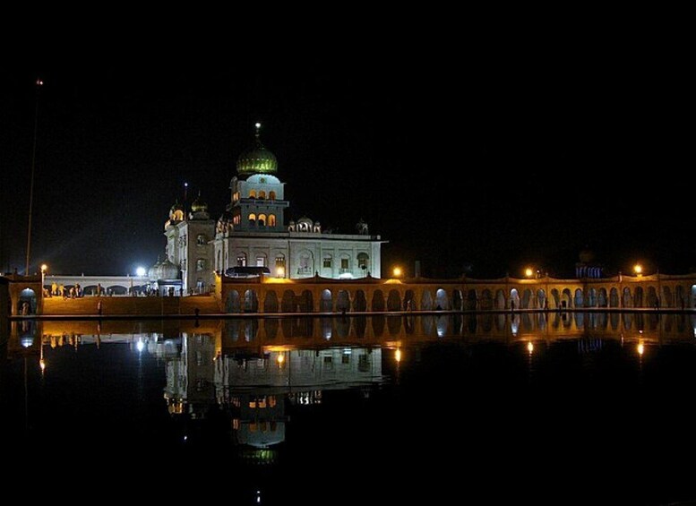 A night view of a large, illuminated building with a dome and arched windows, reflecting on a calm body of water. 5