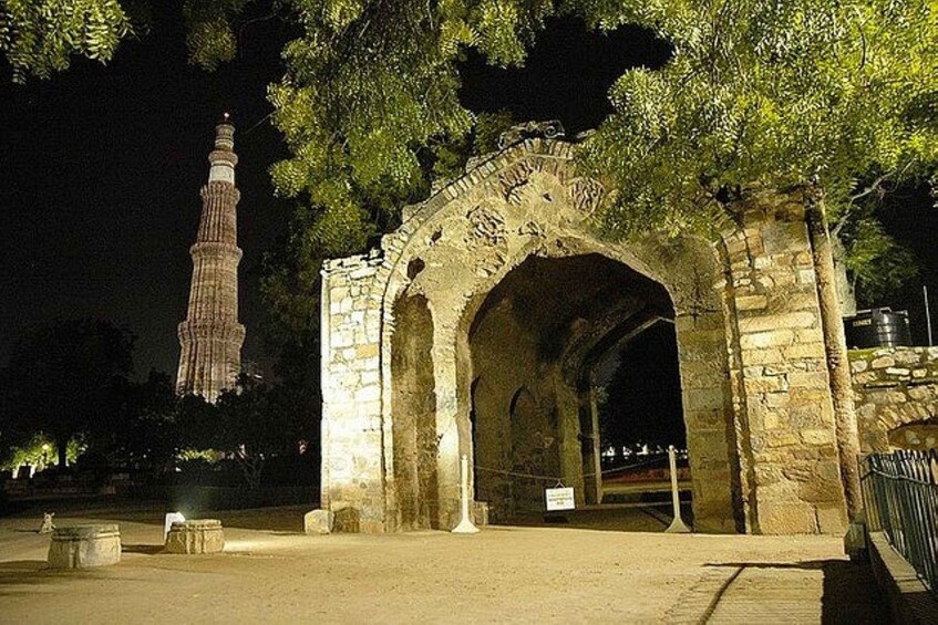 An ancient stone archway with intricate carvings, a tall minaret in the background, and a well-lit pathway leading through it. 3