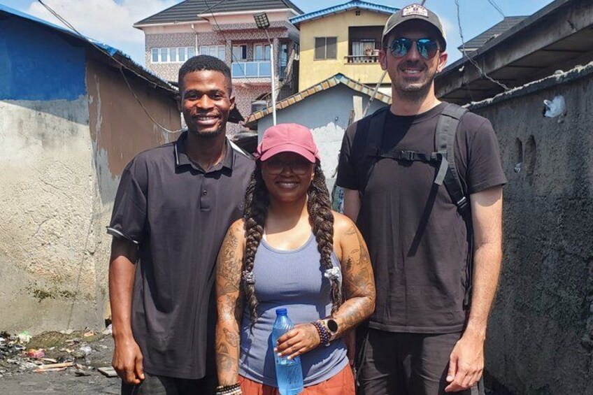 Tres personas de pie en un callejón urbano, con edificios al fondo. 2