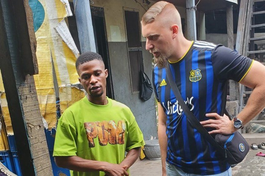 Two individuals standing in an urban alleyway with buildings and a ladder in the background. 4