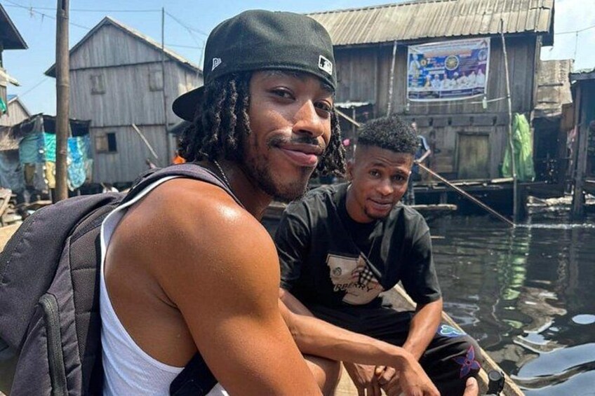 Two people on a boat in a waterway with wooden buildings in the background. 1