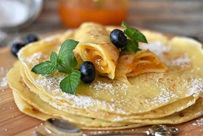 A stack of crepes topped with blueberries, mint leaves, and powdered sugar. 2