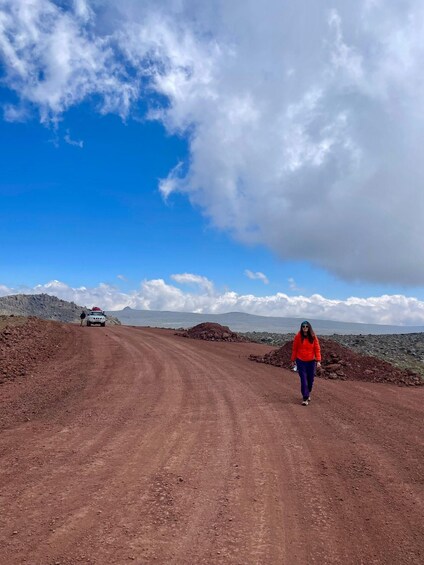 A person walking on a dirt road with a car in the distance and mountains in the background. 5