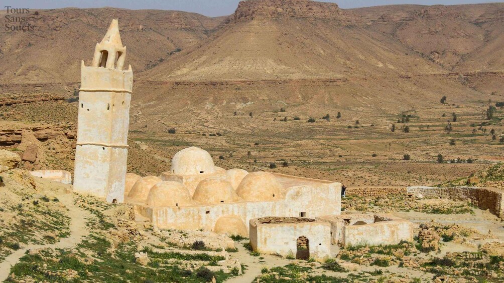 A desert landscape with a historical building featuring a minaret and dome structures. 2
