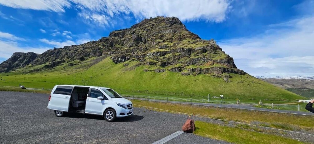 A white van parked on a road with a mountainous landscape in the background. 4