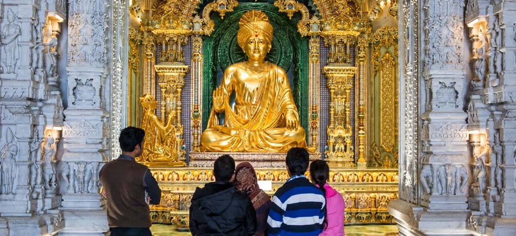 A golden Buddha statue in a temple with intricate carvings and a group of people observing it. 3