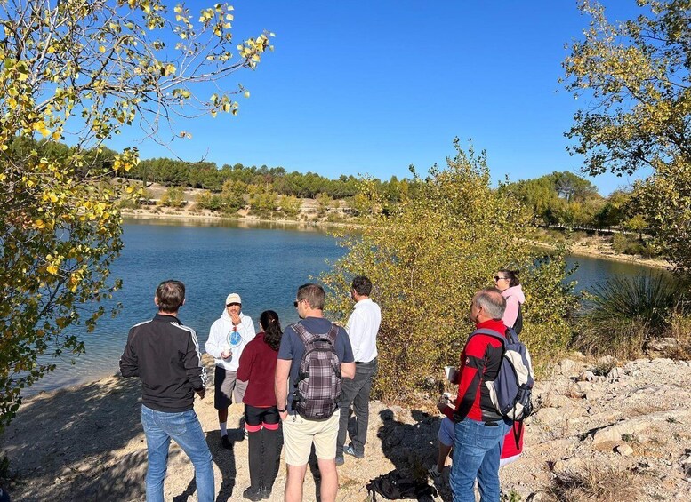 A group of people standing by a lake with trees and a clear sky. 3
