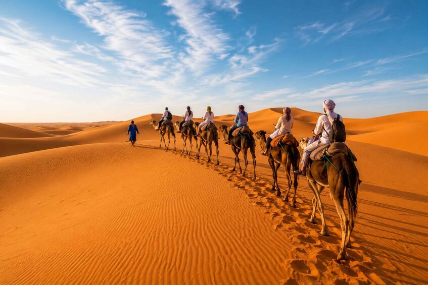 A group of people riding camels across a desert landscape with sand dunes. 1