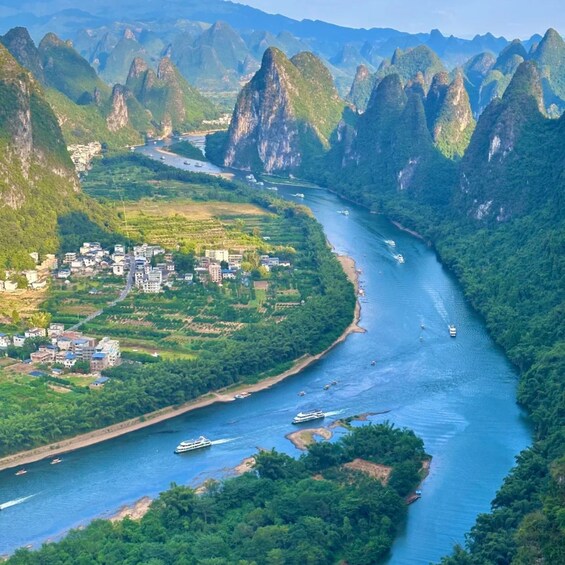 A river winding through a mountainous landscape with a town on the riverbank and boats on the water. 3