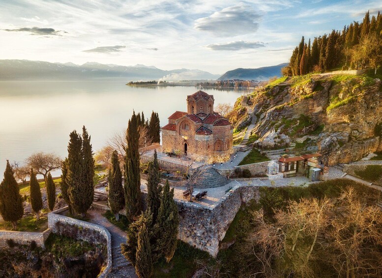 A historic church on a hillside overlooking a lake, with mountains in the background. 1