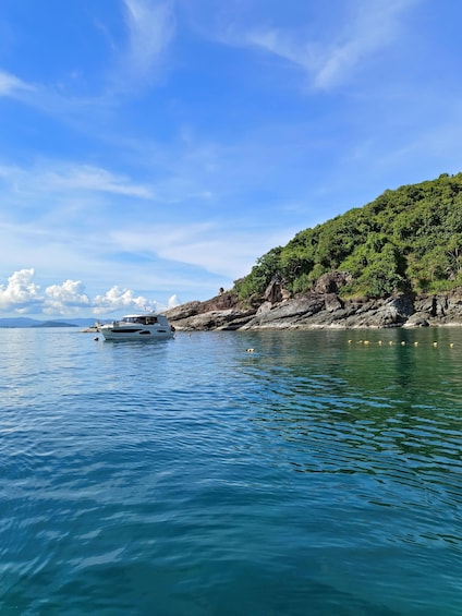 A boat on calm water near a rocky shore with a forested hill. 3