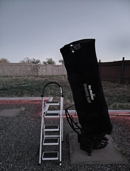 Un telescopio con una etiqueta, una escalera metálica y un suelo de grava. 3