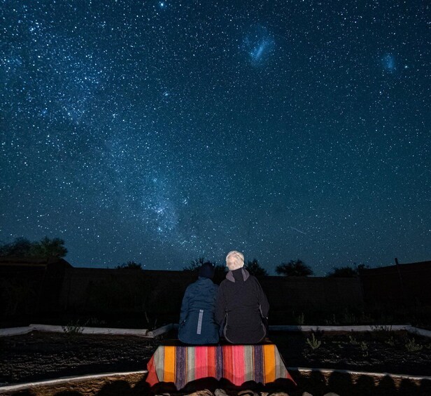 Two people sitting on a blanket under a starry night sky. 5