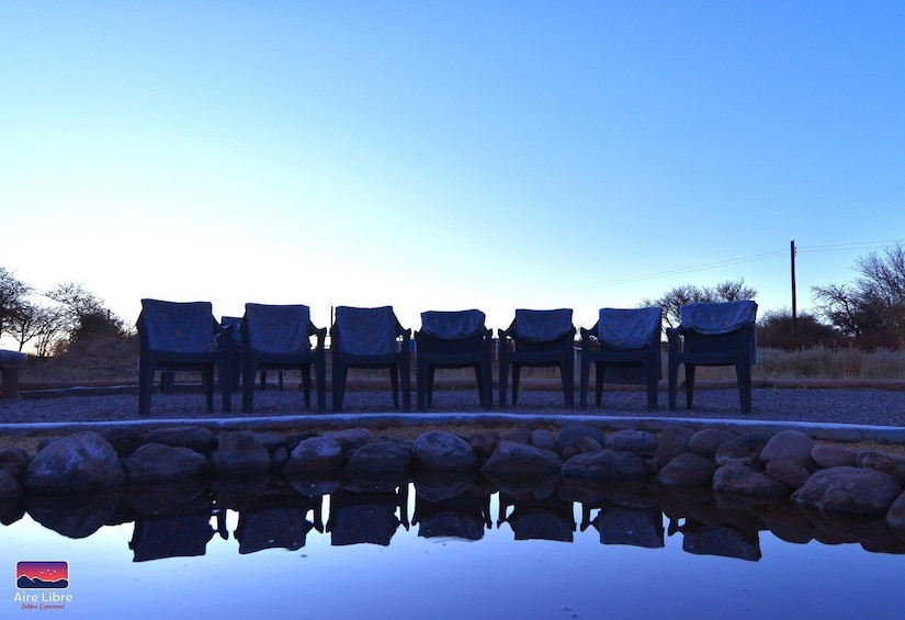 A row of chairs by a calm water body with a clear sky. 3