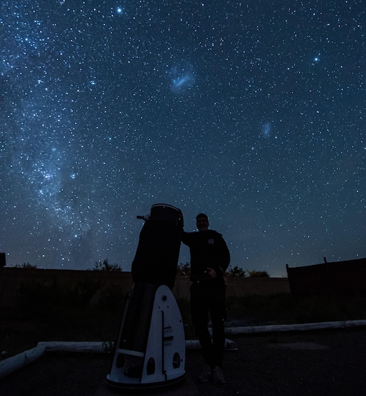 A person standing next to a telescope under a starry night sky. 1