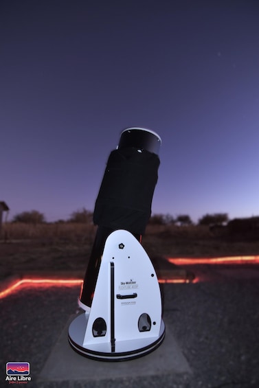 A telescope with a white body and black top, labeled "Sky Watch FlexiScope," set up outdoors with a clear sky in the background. 4