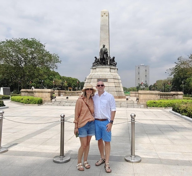 A couple standing in front of a monument with a tall obelisk and statues. 1