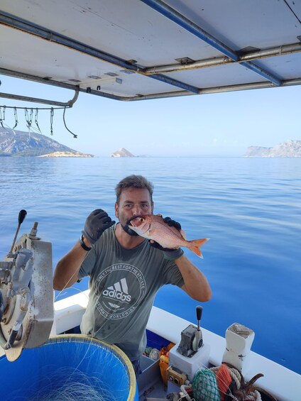 A person holding a fish on a boat with a clear view of the sea and distant land. 2