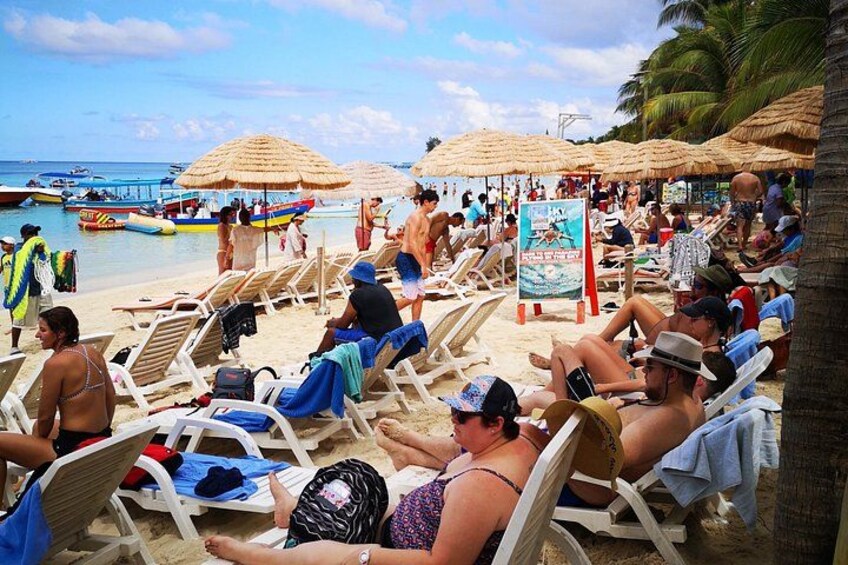 A beach with people sunbathing, lounge chairs, and thatched umbrellas. 2