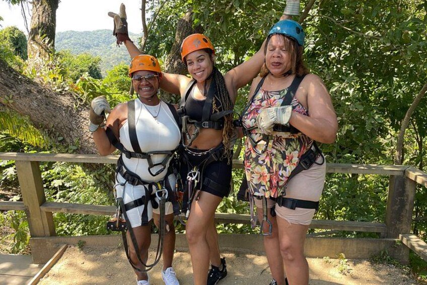 Three people in harnesses and helmets, standing on a wooden platform with greenery in the background. 4