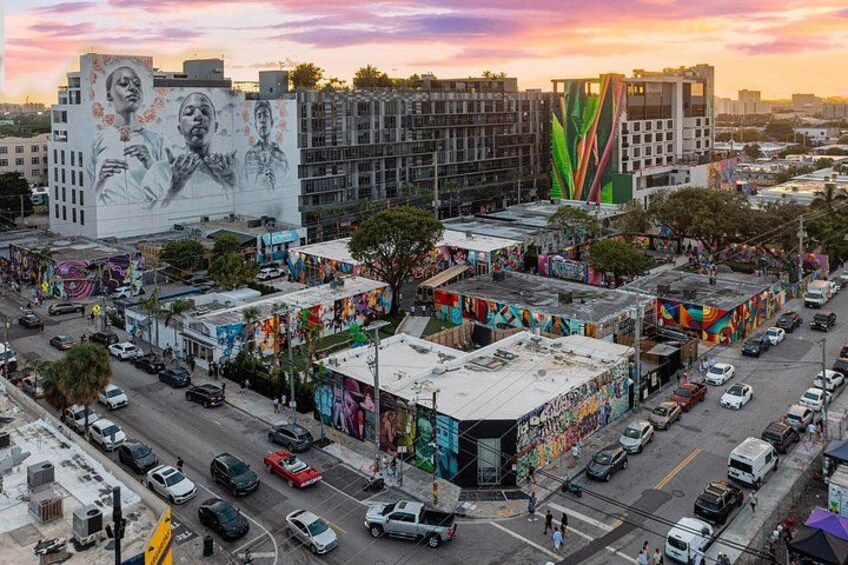 A busy urban street with colorful murals on buildings, a large mural on a building, and a tall building with a green and red design. 3