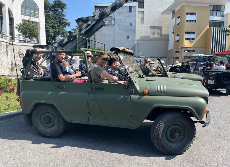 A military vehicle with a mounted cannon, passengers, and urban buildings in the background. 3