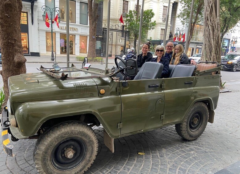 A green military-style jeep parked on a cobblestone street with a group of people inside. 2