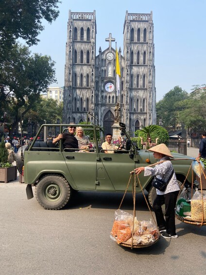 A vintage military jeep with passengers and a vendor selling snacks in front. 4