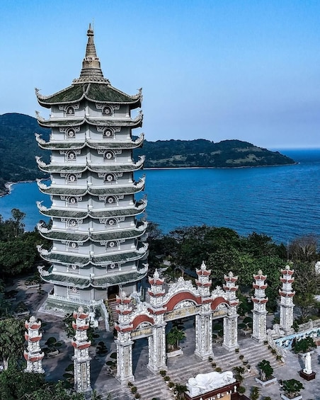 A multi-tiered pagoda with intricate designs, surrounded by traditional architecture and a scenic coastal landscape. 2