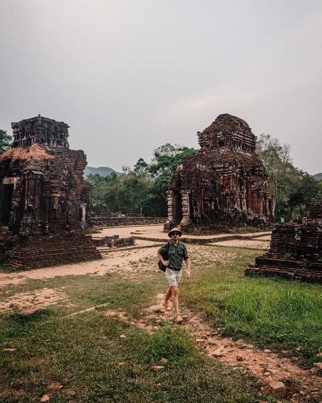 A person walking among ancient ruins with overgrown grass and trees in the background. 4