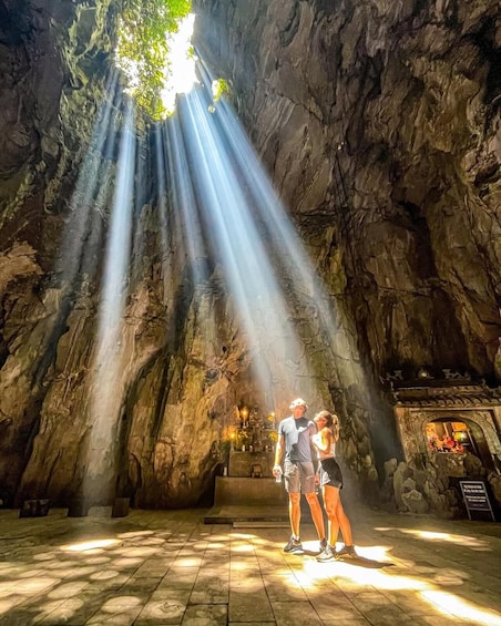 A cave with sunlight streaming through rock formations, a couple standing in the center, and a shrine to the right. 5