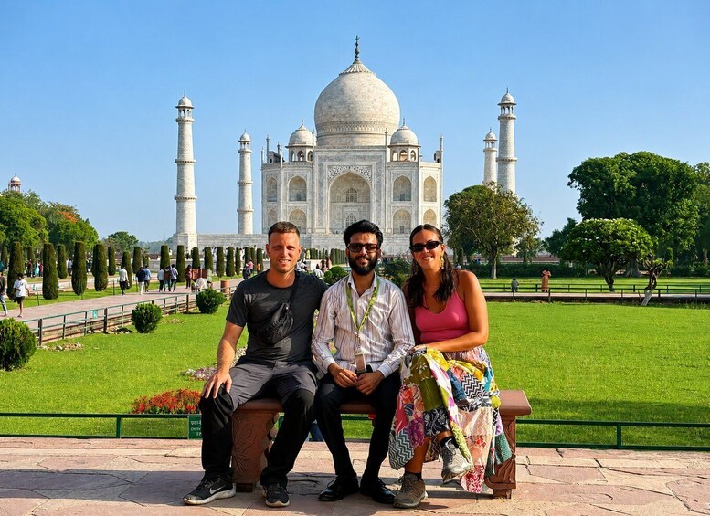 Three people sitting on a bench with the Taj Mahal in the background. 2