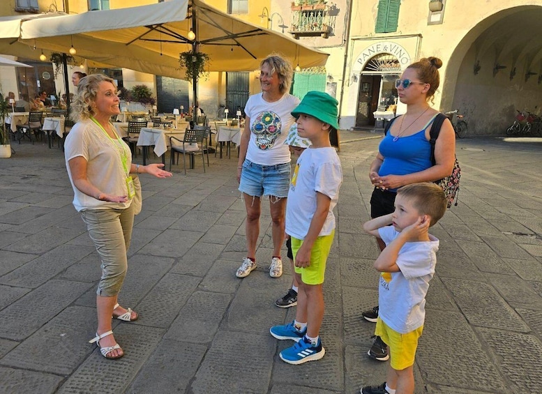 A group of people standing in a public square with outdoor seating and a building labeled "PANE & VINO" in the background. 1