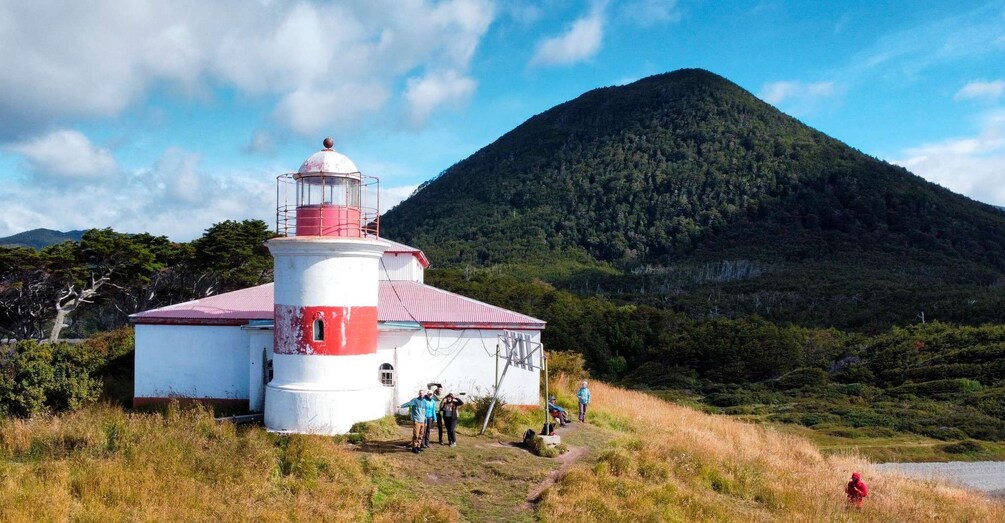 A lighthouse with a red and white structure, surrounded by a grassy area and a mountain in the background. 1