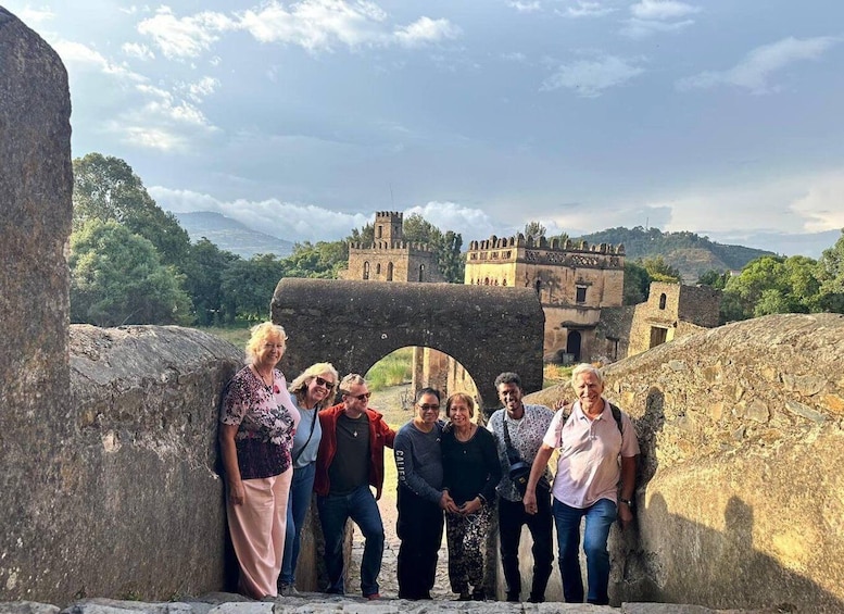 A group of people standing in front of a historical stone archway with a castle in the background. 1