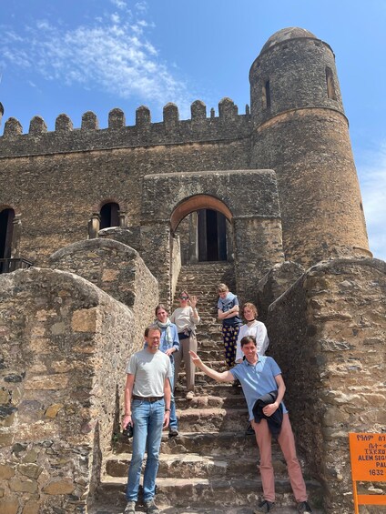 A group of people standing in front of a historic stone castle with a large tower and arched entrance. 2