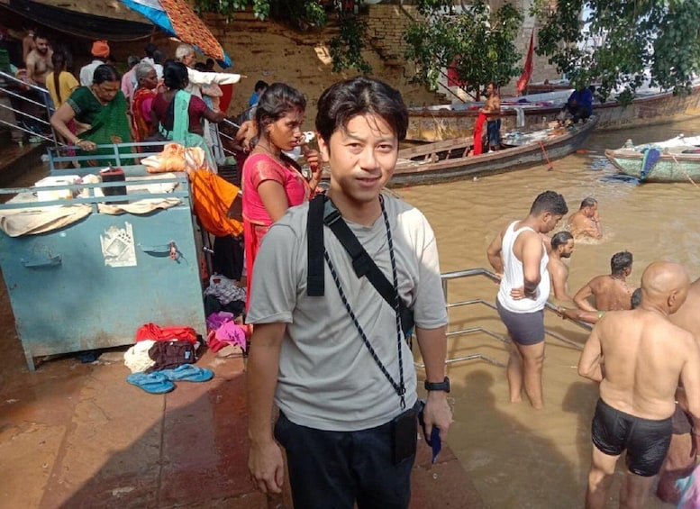 A man standing in a river with boats and people around. 5
