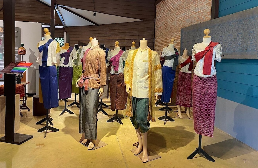 Mannequins displaying traditional garments in a shop with a brick wall and a display table. 1