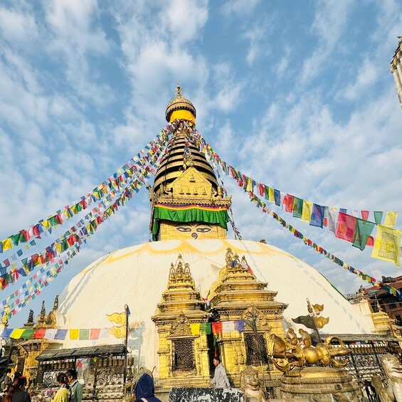 En stor, vit stupa med färgglada böneflaggor, gyllene statyer och en detaljerad arkitektur. 5
