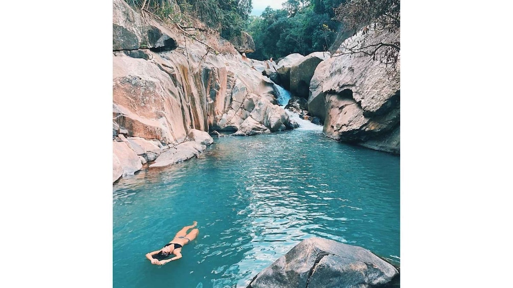 A person floating in a clear blue river surrounded by rocky terrain and a waterfall. 3