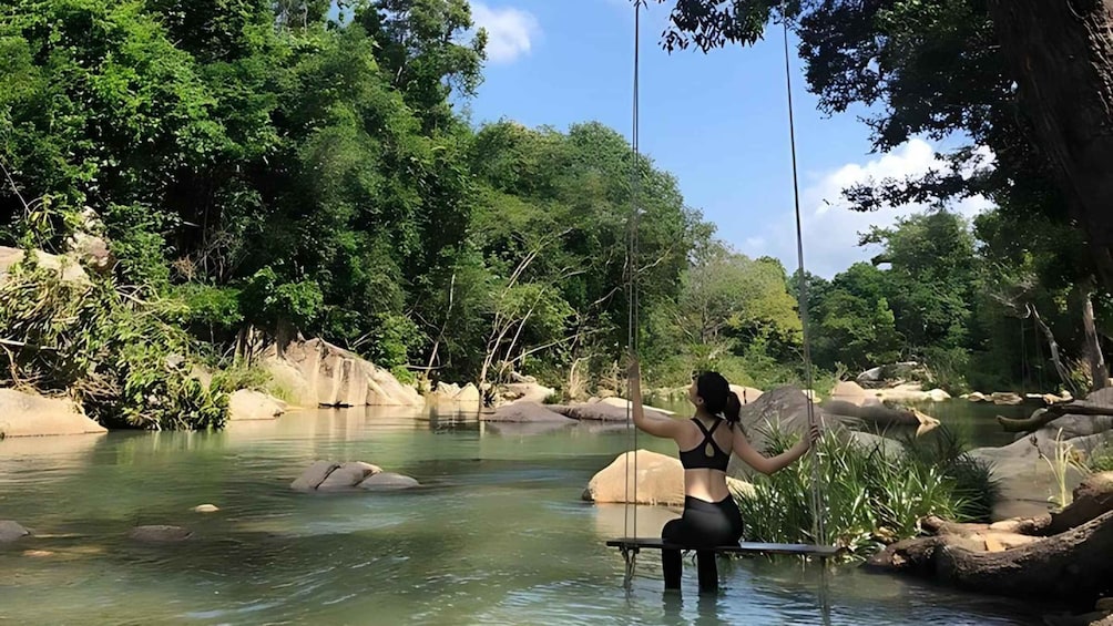 A person sitting on a swing in a river surrounded by rocks and greenery. 2