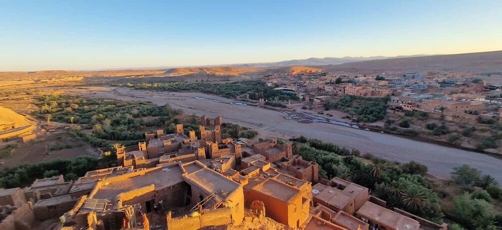 A desert landscape with a river, traditional buildings, and distant mountains. 3