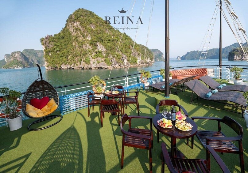 A boat deck with outdoor seating, a view of a mountainous island, and the name 'REINA' on the railing. 2